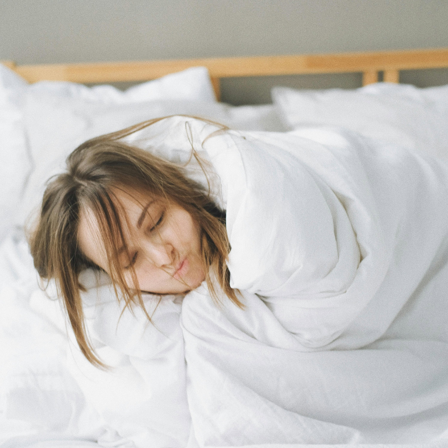 Schläfrige Frau im Bett mit mit Bettdecke zum Kinn gezogen