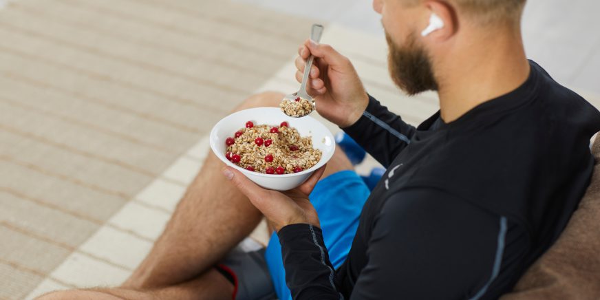 Junger Sportler sitzt auf Sofa und isst Granola