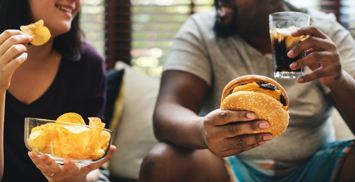 Zum Abnehmen ist ein Kaloriendefizit entscheidend – Tees alleine können eine ungesunde Ernährung nicht ausgleichen Paar-auf-der-Couch-isst-Fastfood