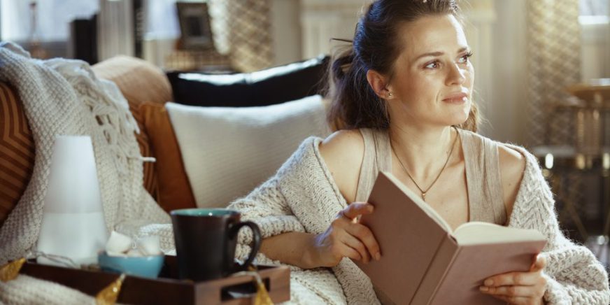 Frau-mit-Buch-in-der-Hand-und-Tee-auf-der-Couch