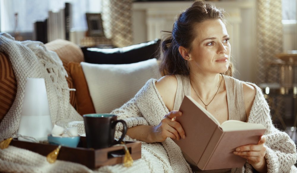 Frau-mit-Buch-in-der-Hand-und-Tee-auf-der-Couch